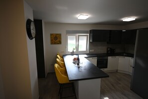 A modern kitchen with white cabinets, a black countertop, and a yellow chair. - House Ivana (Pula)