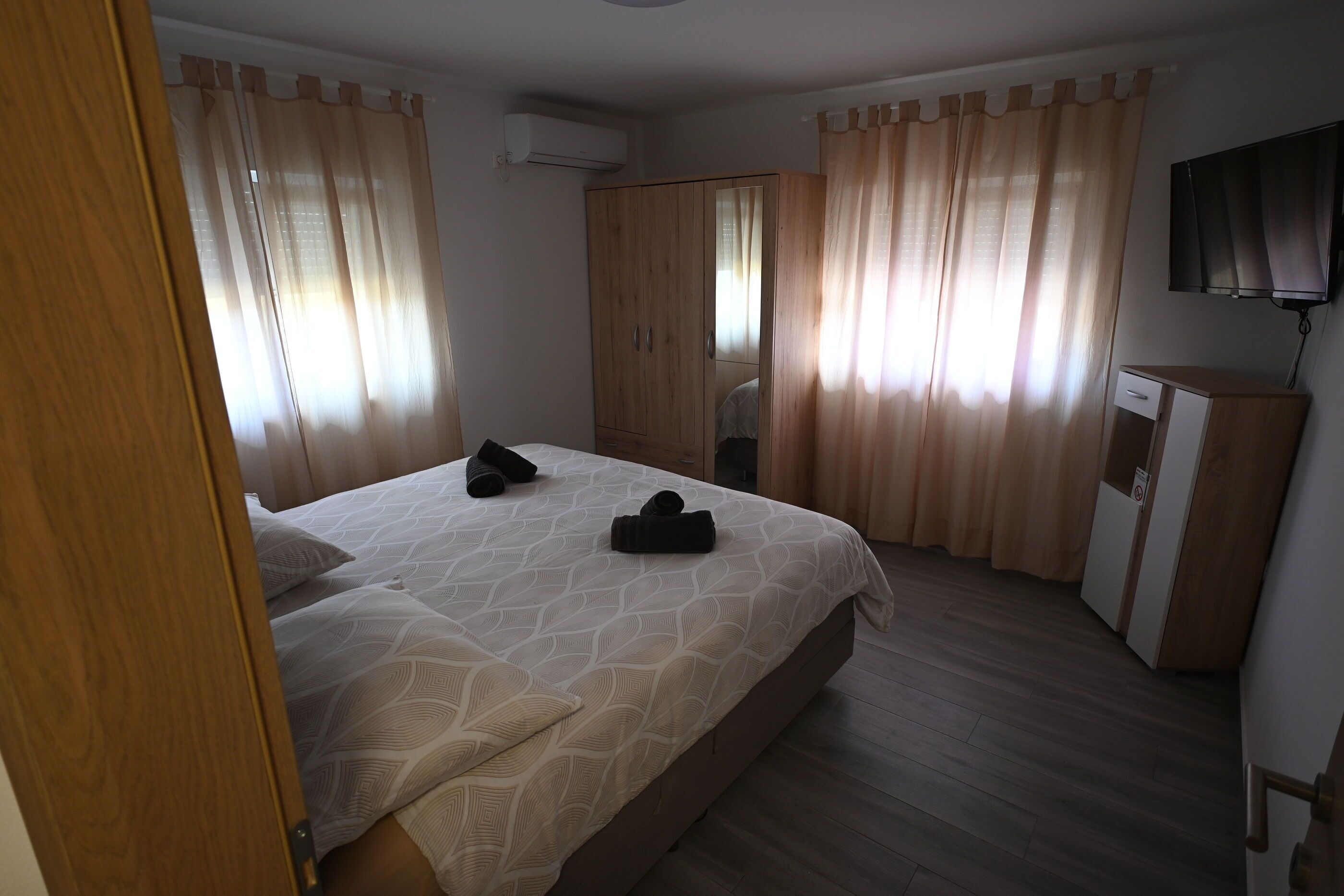 A bedroom with a bed, curtains, a wardrobe, a TV, and a desk.