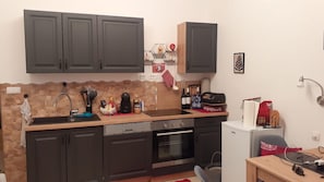A compact kitchen with dark cabinets, a stone backsplash, a built-in oven, and a small refrigerator. - Apartment Marina (Rab)
