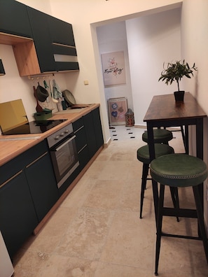 A compact kitchen with dark cabinets, a wooden countertop, and a small dining area with two stools. - Apartment Marina (Rab)