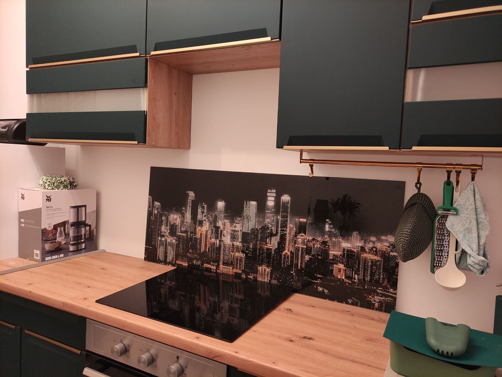 A kitchen with a black stovetop, wooden countertop, and a cityscape wall art.