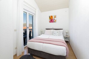Ein Schlafzimmer mit einem Bett, einem Nachttisch, einer Lampe, einem Gemälde und einer Glastür, die zu einem Außenbereich führt.
