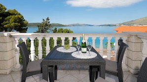 Ein Balkon mit Tisch, Stühlen, einer Champagnerflasche und einer Schale mit Trauben.