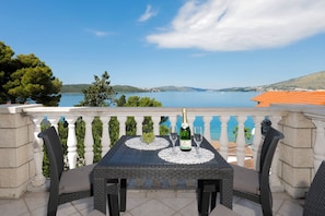 Ein Balkon mit Tisch, Stühlen, einer Champagnerflasche und einer Schale mit Trauben.