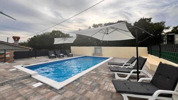Ein Swimmingpool mit Liegestühlen und Sonnenschirmen, umgeben von Steinplatten.