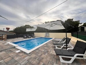 A swimming pool with lounge chairs and umbrellas, surrounded by stone tiles. - House Aida (Sveta Nedelja)