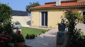 Ein gelbes Gebäude mit rotem Ziegeldach, einer Tür und einem kleinen Garten mit Topfpflanzen.