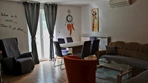 Ein Wohnzimmer mit einer Couch, einem Couchtisch, einem Esstisch mit Stühlen, einer Wanduhr und einer Klimaanlage.
