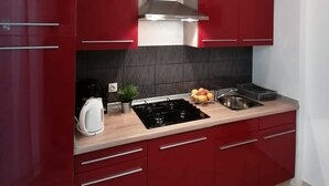 A modern kitchen with red cabinets, a stainless steel range hood, a gas stove, a sink, and a kettle. - Apartments Andreja (Crikvenica)