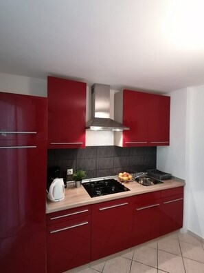 A modern kitchen with red cabinets, a stainless steel range hood, a gas stove, a sink, and a kettle. - Apartments Andreja (Crikvenica)