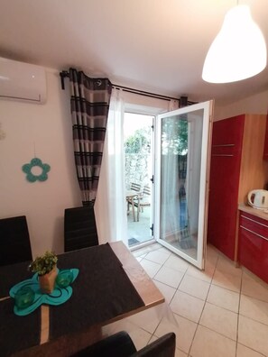 A dining area with a table, chairs, and a potted plant. There is a sliding glass door leading to an outdoor area with a table and chairs. - Apartments Andreja (Crikvenica)