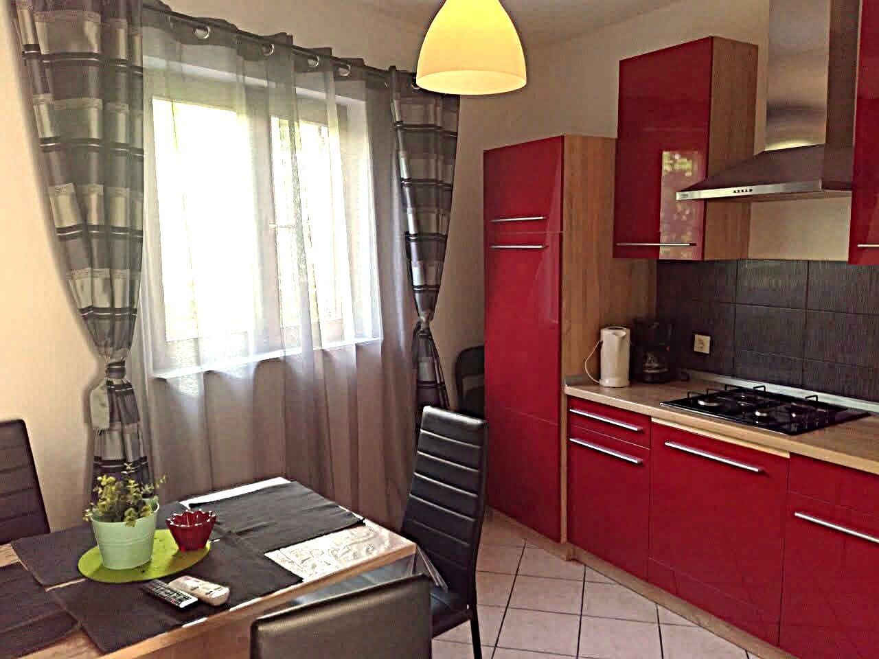 A compact kitchen with red cabinets, a gas stove, and a dining area with a table and chairs.