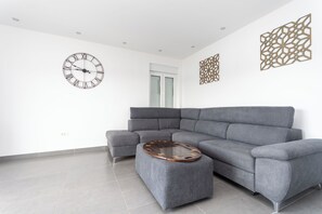 Ein modernes Wohnzimmer mit einer grauen Eckcouch, einem runden Couchtisch, einer Wanduhr und dekorativer Wandgestaltung.