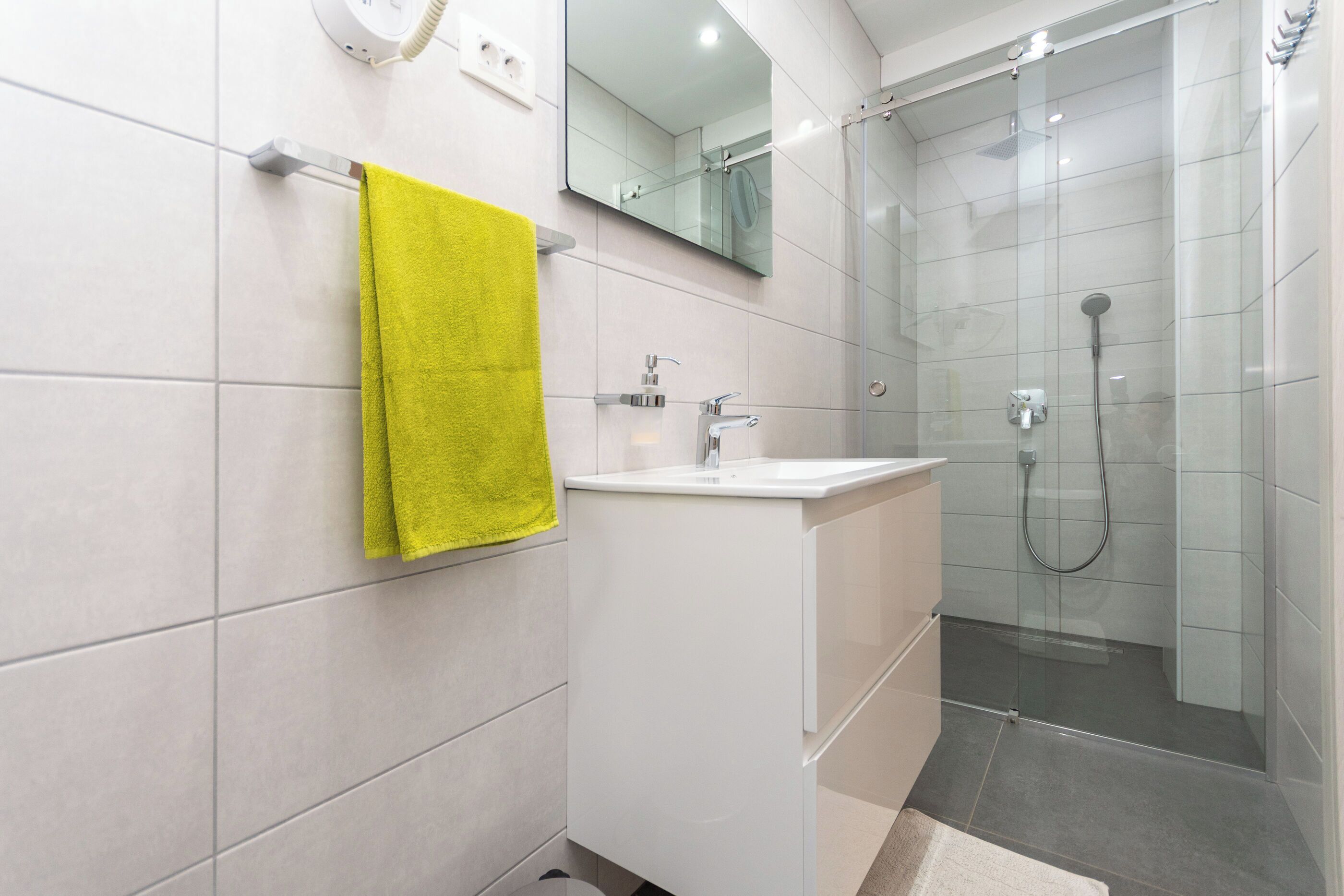 A modern bathroom with a white sink, mirror, and glass shower enclosure.