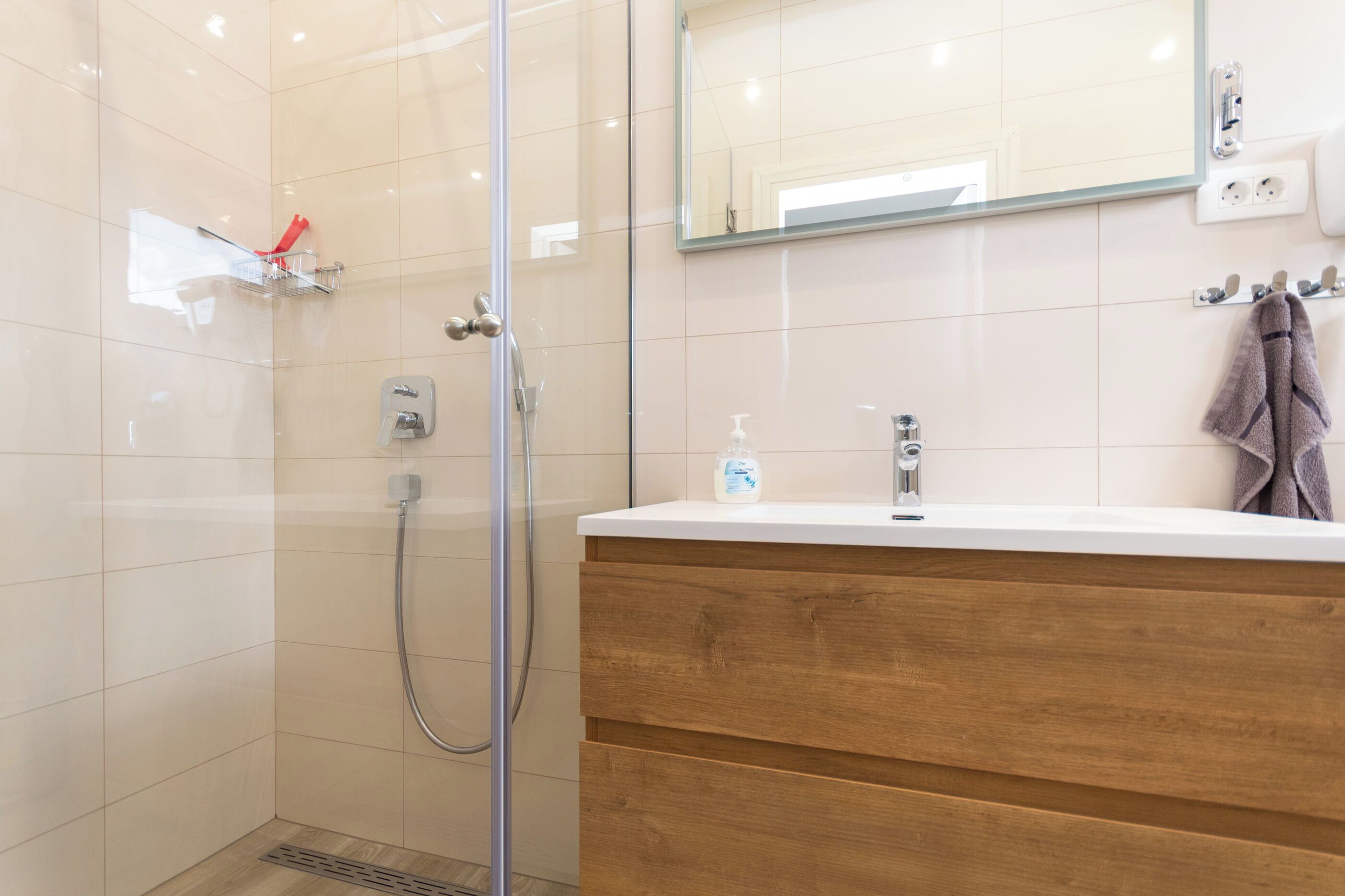 Une salle de bain moderne avec une douche à parois de verre, un meuble-lavabo en bois, un miroir et un porte-serviettes.