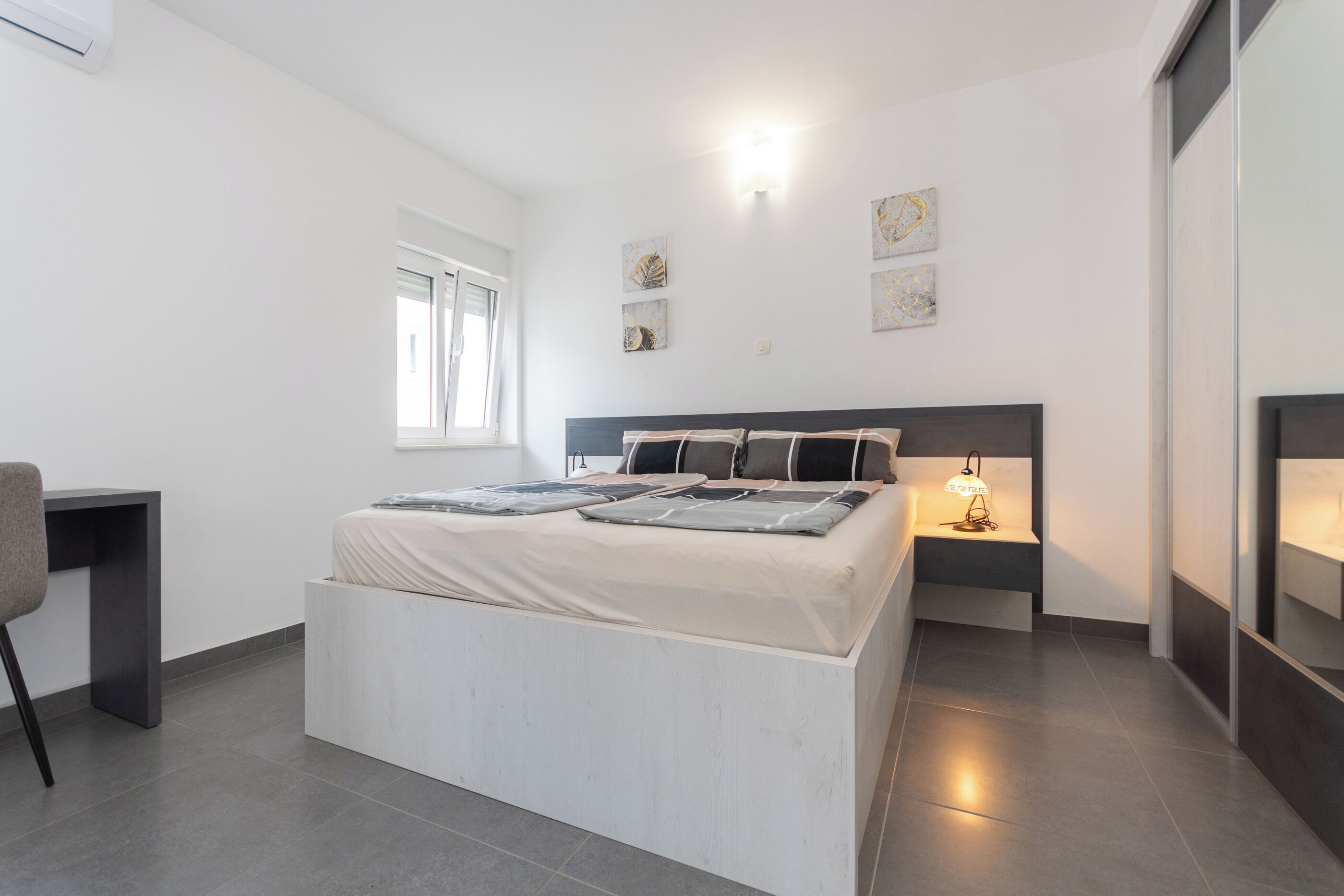 A modern bedroom with a large bed, bedside tables, a desk, and artwork on the walls.