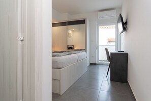 Ein Schlafzimmer mit einem Bett, einem Schreibtisch und einem Stuhl. Eine Schiebetür führt in einen weiteren Raum.