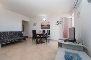 A room with a sofa, dining table, chairs, a TV, and a painting on the wall. - Apartments Luca sea View (Razanac)