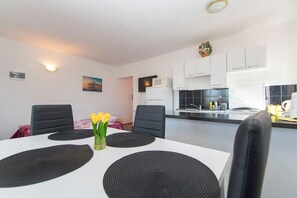 A modern kitchen with white cabinets, a microwave, and a sink. There is a dining table with black placemats and a vase with yellow flowers. - Apartments Luca sea View (Razanac)