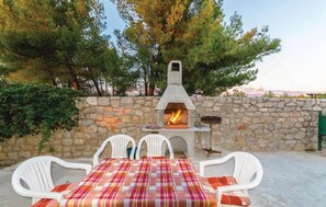 An outdoor patio with a stone wall, a wood-burning pizza oven, and white chairs. - Apartments Luca sea View (Razanac)