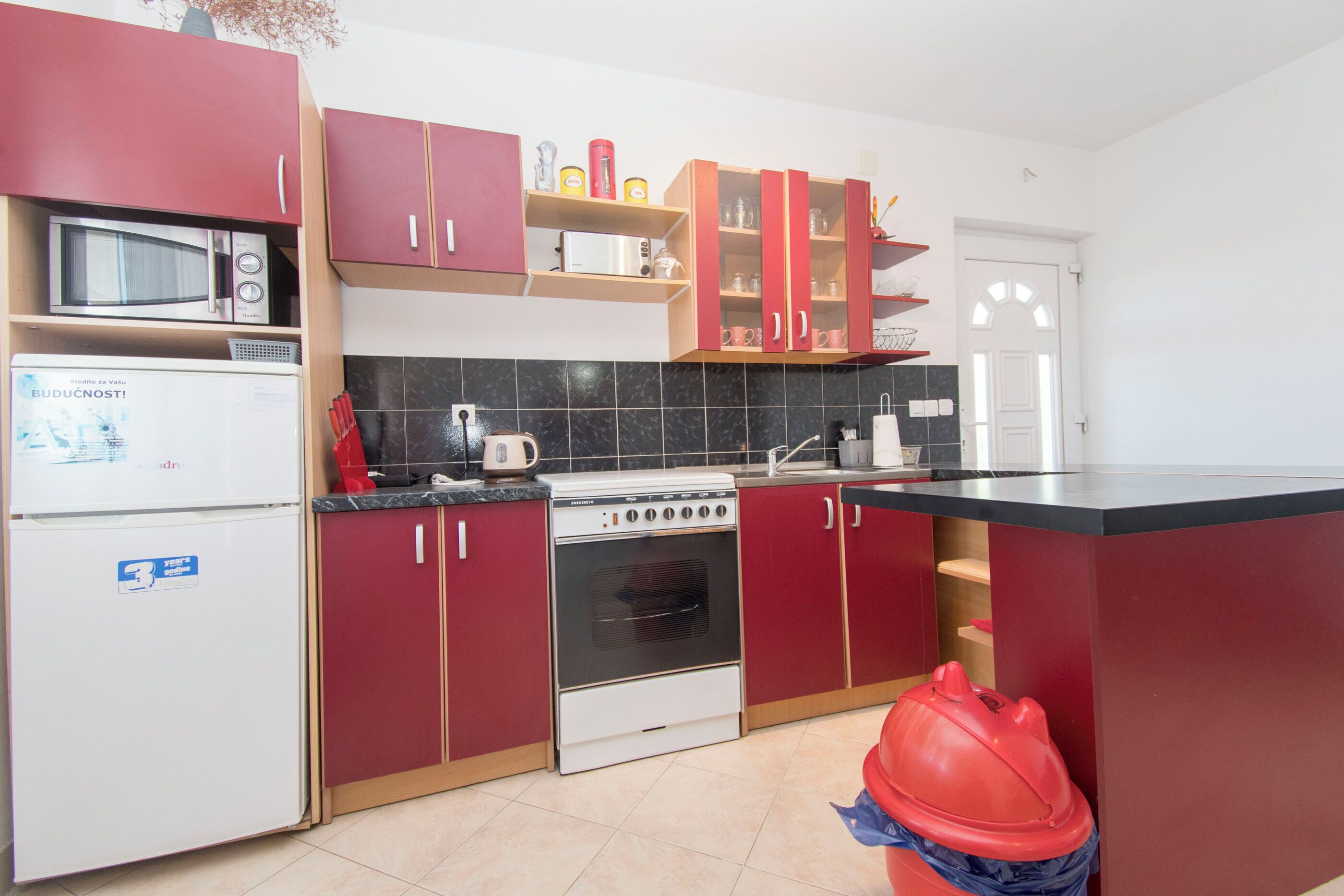A kitchen with red cabinets, a white refrigerator, a stove, and a microwave.