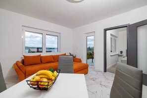 Una sala de estar moderna con un sofá, una mesa de comedor con fruta y vistas a través de amplios ventanales.