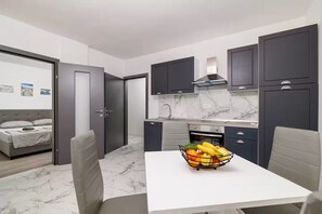 A compact kitchen with dark cabinets, a marble countertop, and a dining area with a fruit bowl. - Apartments Yasmin i Marina (Crikvenica)