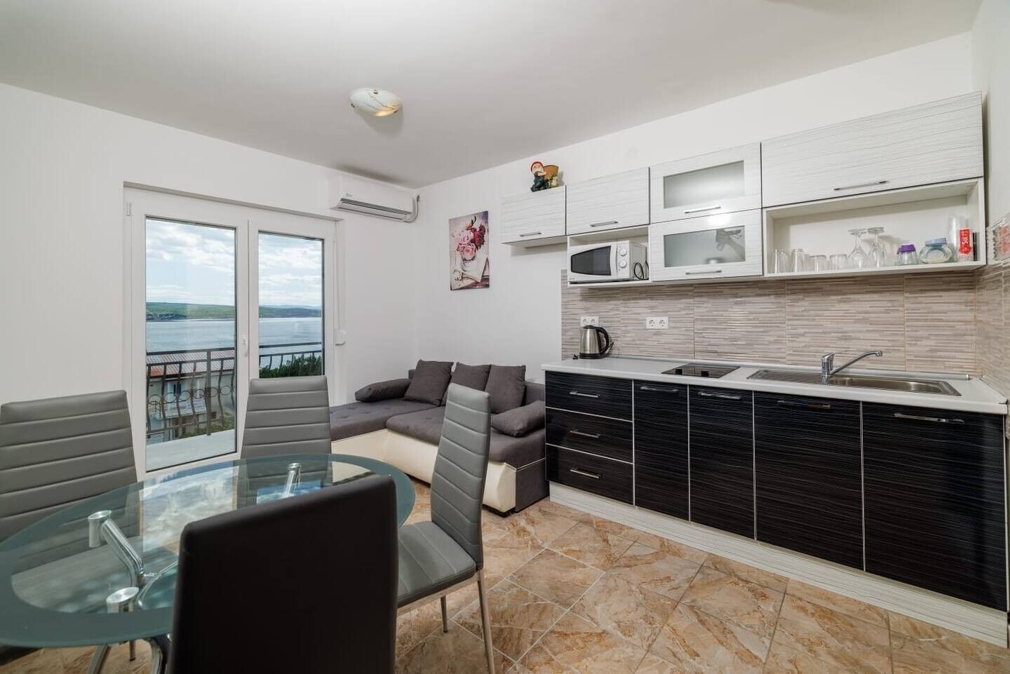 A modern kitchen with a dining area, a sofa, and a view of the sea.