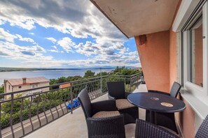 Un balcón con mobiliario de mimbre, vista a un lago y una orilla distante.