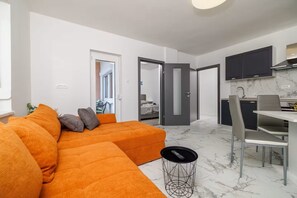 A modern living room with a sectional sofa, a dining area with a table and chairs, and a kitchen with dark cabinets. - Apartments Yasmin i Marina (Crikvenica)