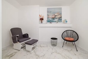 A room with a gray chair, a black wire chair, a small round table, and a painting of boats on the wall. - Apartments Yasmin i Marina (Crikvenica)
