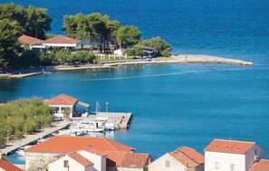 Un puerto costero con barcos amarrados, un muelle que se adentra en el agua y edificios con tejados de teja roja.