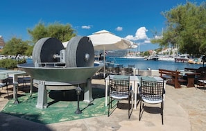 Comedor con mesas y sillas al aire libre, una gran estructura de piedra y vistas al puerto deportivo.