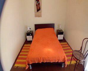 A single bed with an orange bedspread, two bedside tables with lamps, a chair, and a colorful striped rug. - House Veli Iz Oldtown (Zadar)