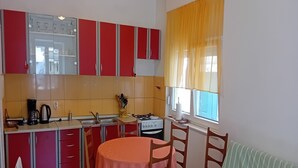 A compact kitchen with red cabinets, a gas stove, and a window with yellow curtains. - House Veli Iz Oldtown (Zadar)