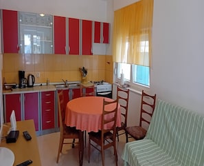A compact kitchen with red cabinets, a gas stove, and a window with yellow curtains. - House Veli Iz Oldtown (Zadar)