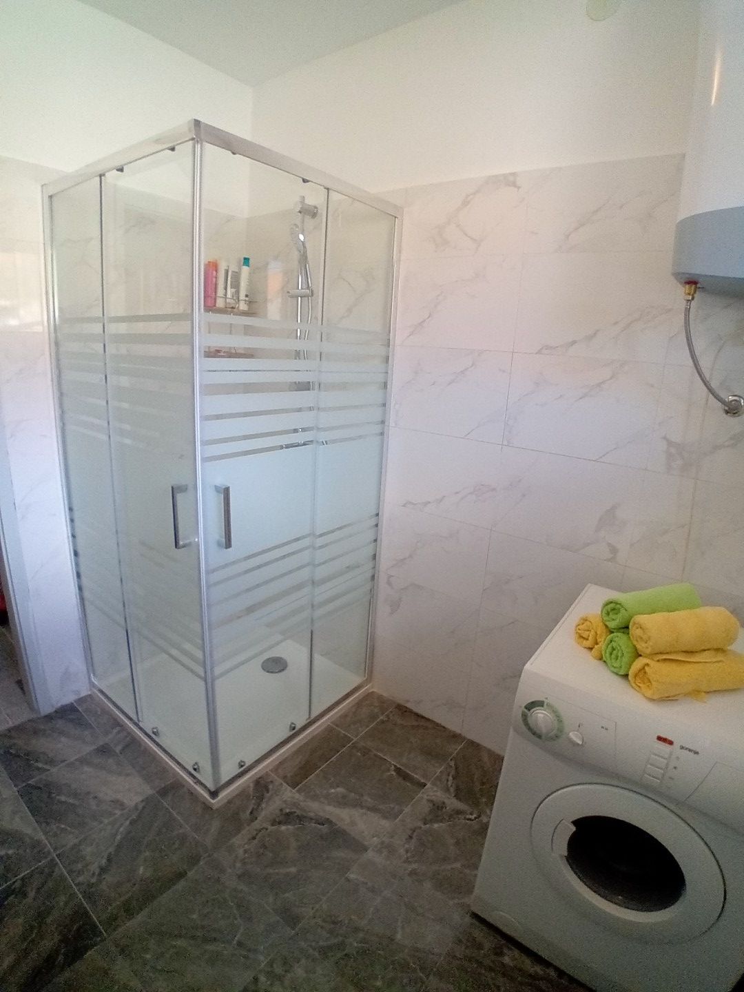 Une salle de bain avec une douche à parois de verre, un lave-linge et un mur recouvert de carreaux de marbre.