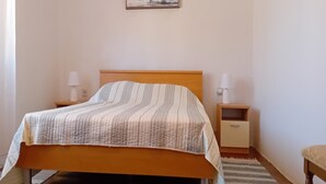 Un dormitorio con una cama, dos mesitas de noche con lámparas, una mesita auxiliar, un cabecero de madera, un cuadro en la pared y una alfombra en el suelo.