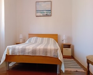 Un dormitorio con una cama, dos mesitas de noche con lámparas, una mesita auxiliar, un cabecero de madera, un cuadro en la pared y una alfombra en el suelo.