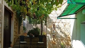 A stone building with a green roof, a small outdoor seating area with two chairs and a table, and potted plants. - House Veli Iz Oldtown (Zadar)