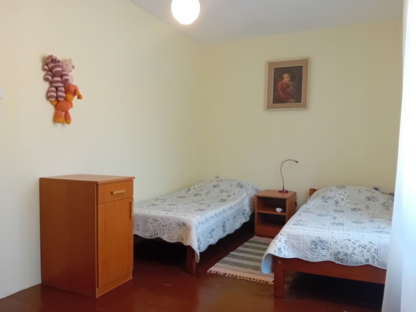 Ein Schlafzimmer mit zwei Einzelbetten, einem Holzschrank, einer kleinen Ablage und einem gerahmten Bild an der Wand.