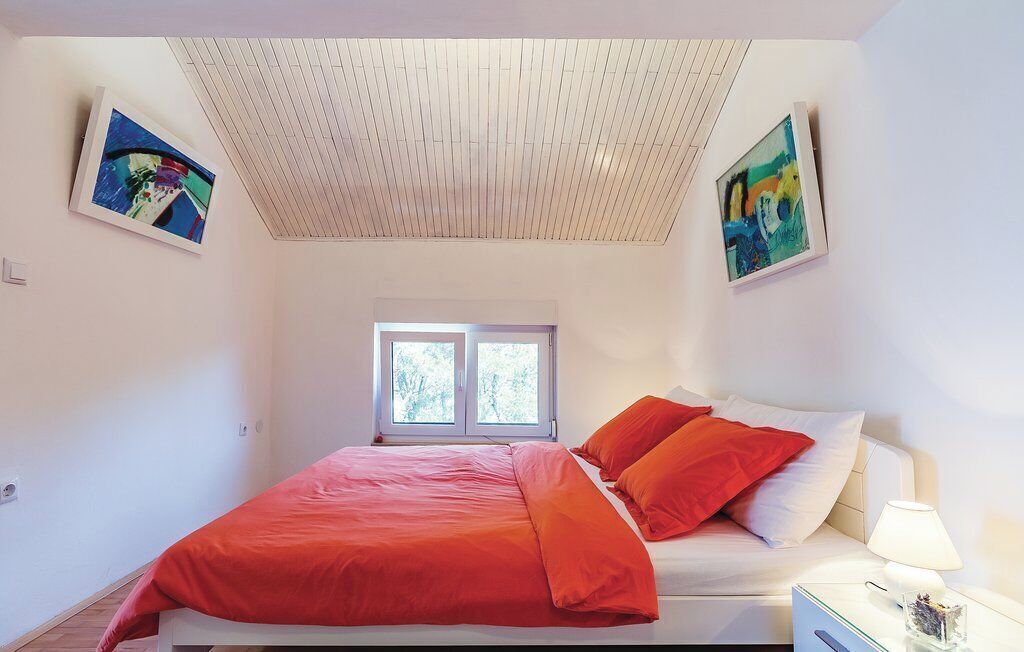 A bedroom with a bed, a window, and two paintings on the walls.