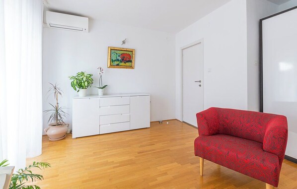 A room with a wooden floor, a white dresser, a red sofa, a potted plant, and a painting on the wall. - House Pineta Art Home (Medulin)