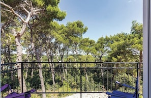 A balcony with a metal railing, two blue chairs, and a view of trees and greenery. - House Pineta Art Home (Medulin)