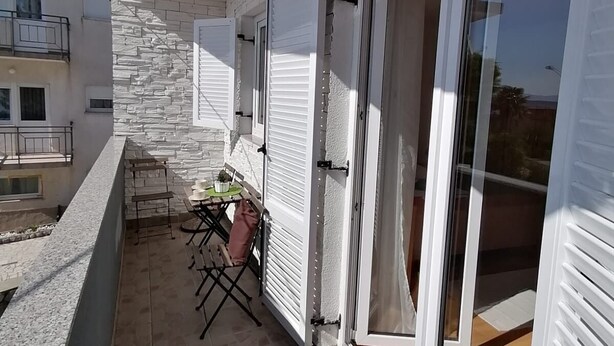 Ein Balkon mit einer Steinsäule, einem Tisch und Stühlen sowie einer Schiebetür aus Glas.