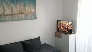 Ein modernes Wohnzimmer mit grauem Sofa, einem Flachbildfernseher und einem Gemälde von Segelbooten.