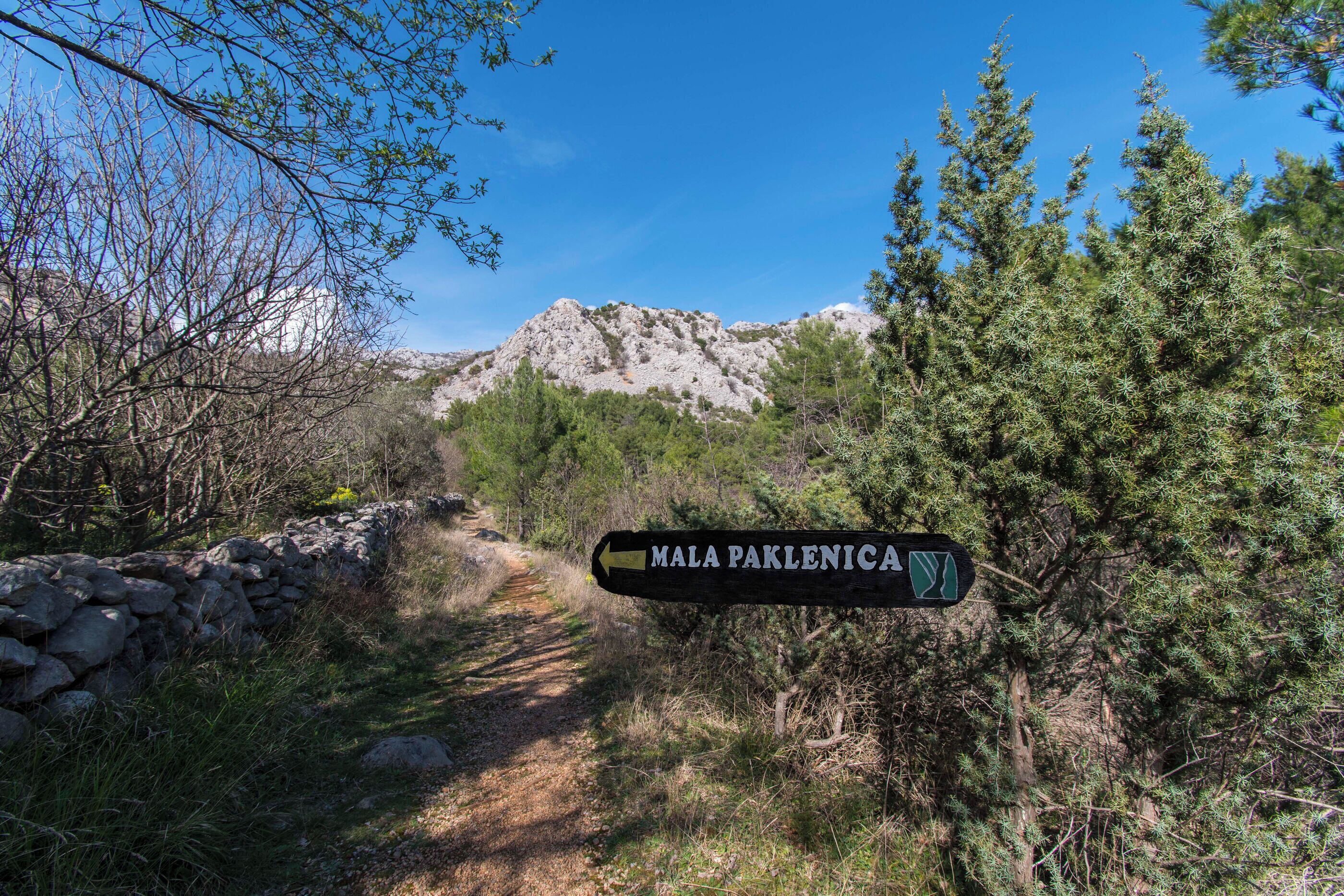 A stone wall, a dirt path, and a sign pointing to Mala Paklenica.