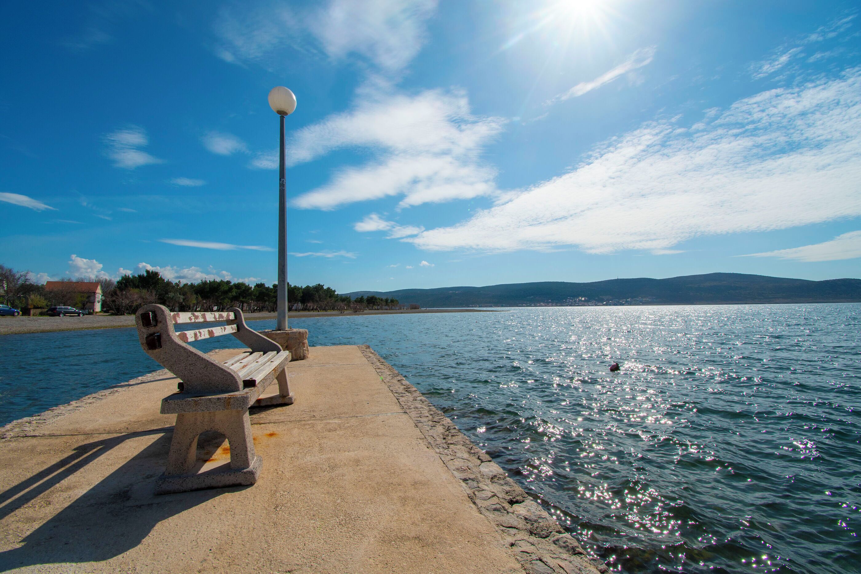 A concrete bench by a body of water with a clear sky.