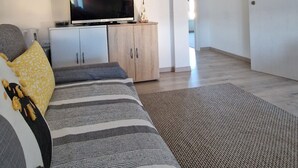 Quarto estilo loft moderno com uma cama grande, uma televisão em um móvel de madeira e vista para a cidade pela janela.