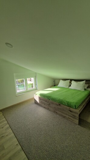 A bedroom with a wooden bed frame, green bedding, a small window, and a carpeted floor. - Apartment By the sea (Dobrinj)